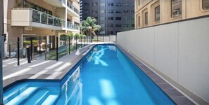 A modern indoor swimming pool with clear blue water, surrounded by a white wall and a glass balcony on one side. - Highlife on Grenfell - 3BR, Wifi, Workspace (Adelaide)