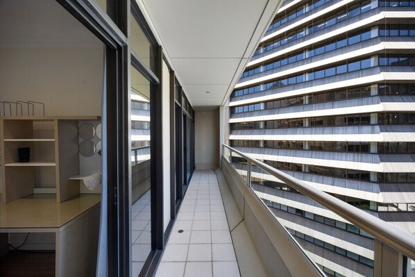 A modern building with a glass facade, a balcony with a metal railing, and a tiled floor.