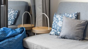 Ett modernt vardagsrum med en grå soffa, blått blommönstrat prydnadskuddar, en blå sittpuff och ett litet träbord.