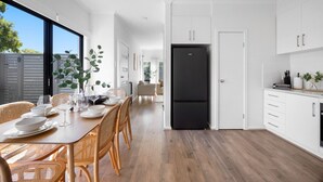 Een moderne keuken met witte kasten, een zwarte koelkast, en een eethoek met rieten stoelen en een houten tafel.