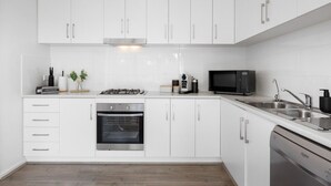 Een moderne keuken met witte kasten, een gasfornuis, een oven, een magnetron en een vaatwasser.