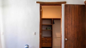 Ein kleines Zimmer mit einem Holzschrank, einem Nachttisch mit Lampe und einer Steckdose.