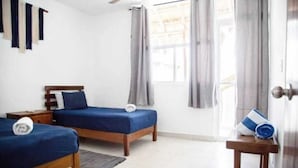 Ein Hotelzimmer mit zwei Betten, einem Holzkopfstück, einem kleinen Tisch und einem Fenster mit Vorhängen.