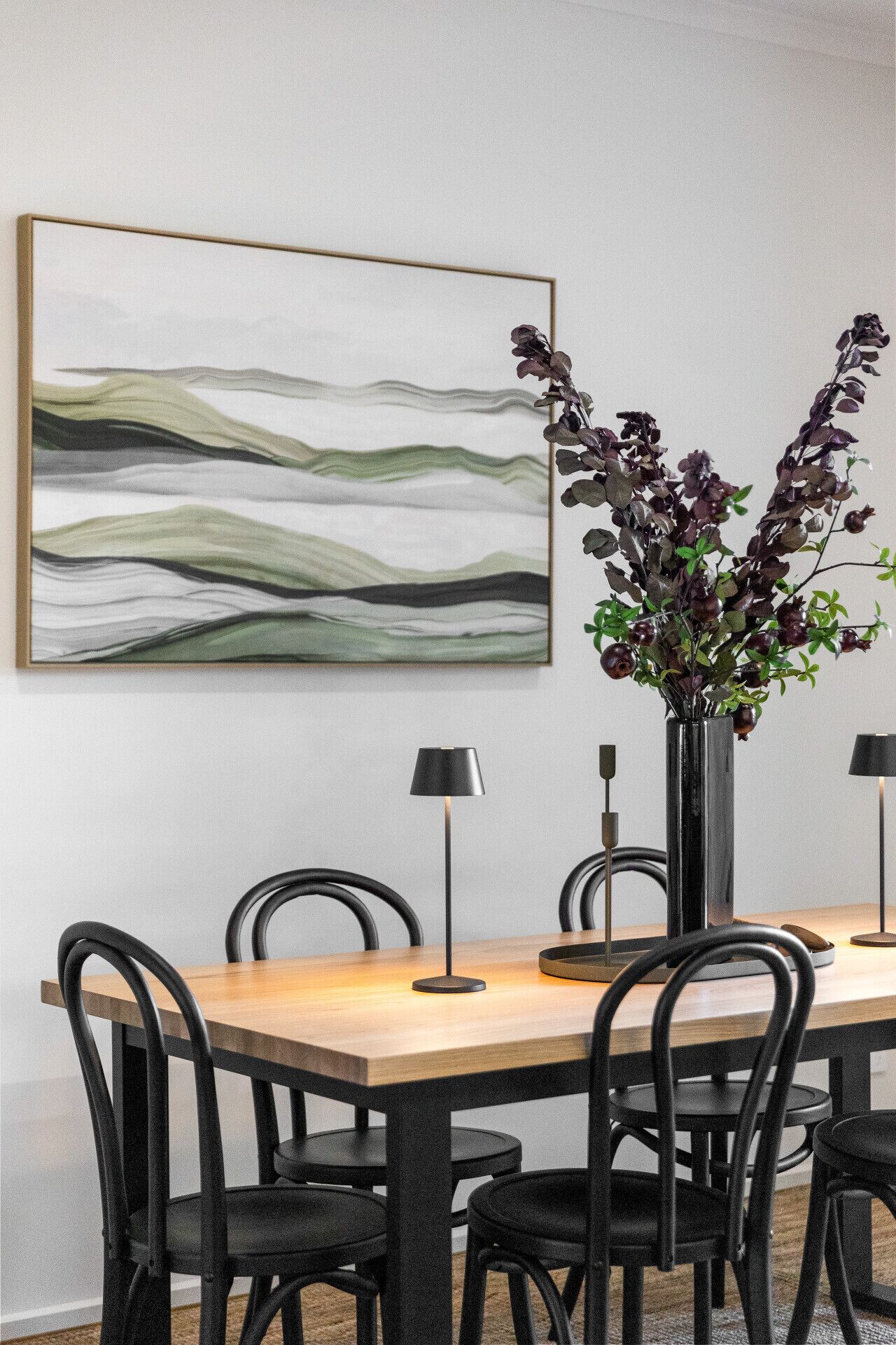 Un coin repas avec une table en bois, des chaises noires, un vase avec des fleurs violettes et un tableau abstrait moderne accroché au mur.
