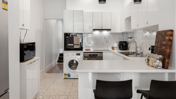 A modern kitchen with white cabinets, a built-in washer and dryer, a coffee maker, and a wooden cutting board.