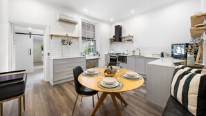 Eine moderne Küche mit weißen Schränken, ein Essbereich mit einem runden Tisch und eine Wohnbereich mit einer Couch und einem Fernseher.