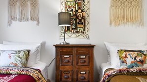 Une chambre avec deux lits, une table de chevet en bois, une lampe et des décorations murales en macramé.