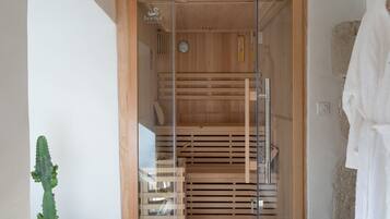 A sauna with wooden benches and a glass door, a clock on the wall, and a towel rack to the right.