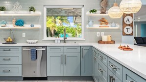 A modern kitchen with grey cabinets, a stainless steel dishwasher, and a window with a view of greenery. - 6BR Htd Pool, Tiki Hut, Mini golf, 8 min to Beach (Bradenton)