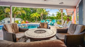 A covered outdoor area with a pool, wicker furniture, and tropical plants. - 6BR Htd Pool, Tiki Hut, Mini golf, 8 min to Beach (Bradenton)
