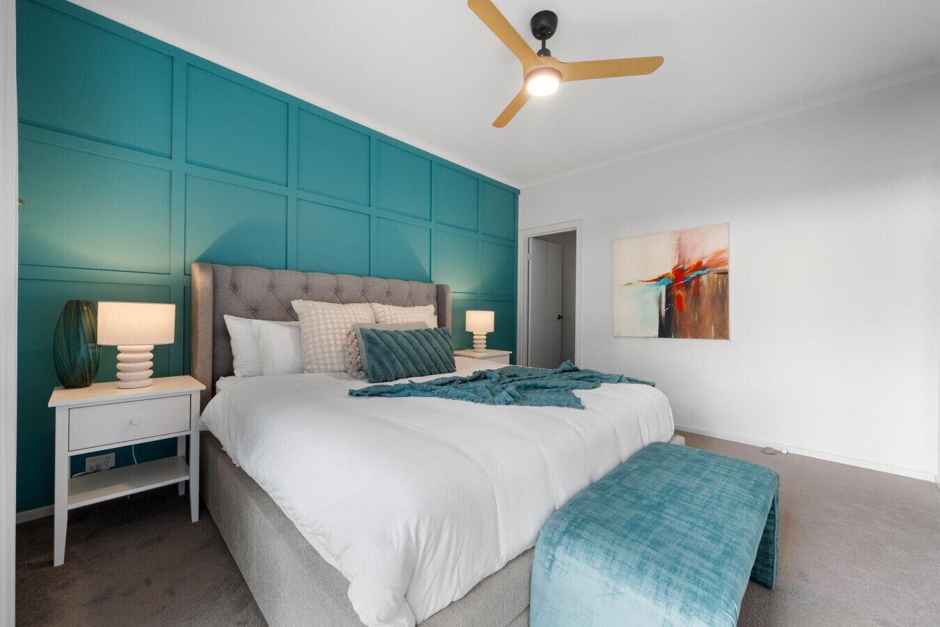 A bedroom with a large bed, two bedside tables, a ceiling fan, and teal accent walls.