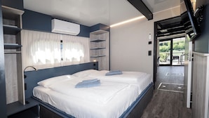 Une chambre moderne dotée d’un grand lit, d’un système de climatisation intégré et offrant une vue sur l’espace extérieur.