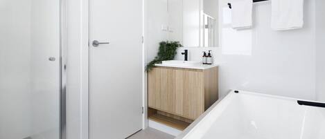 A modern bathroom with a glass shower door, a wooden vanity, a white bathtub, and a mirror above the sink.