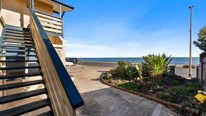 A coastal property with a staircase leading to a balcony overlooking the sea, a garden with cacti, and a parked car. - Horizon 235—Seaview Hideaway on the Esplanade (Glenelg North)
