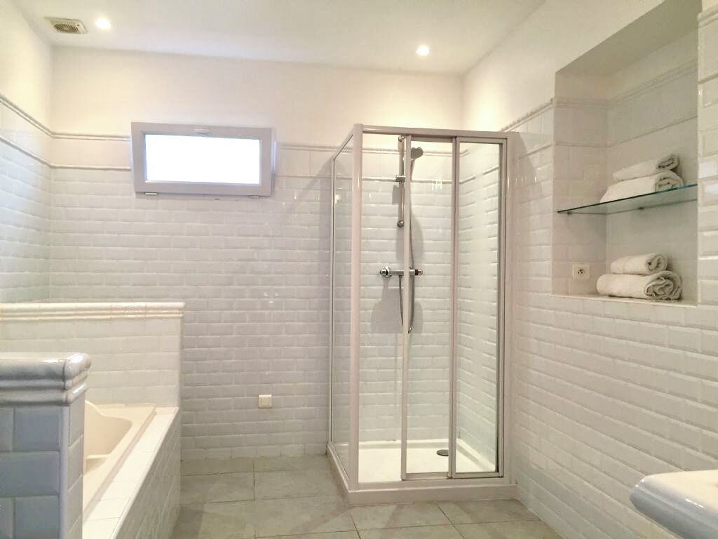 A bathroom with a glass-enclosed shower, a bathtub, and a shelf with towels.