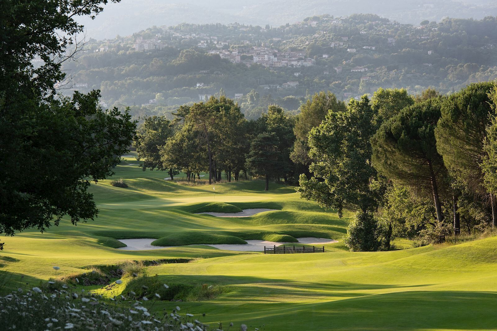 A golf course with sand bunkers, trees, and a distant town.