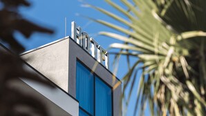 A modern hotel building with a prominent "HOTEL" sign on the roof, large windows, and a palm tree in the background. - Hotel Siel (Durrës)