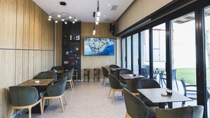A modern restaurant interior with wooden panel walls, a large TV screen, and a mix of dark and light chairs around tables. - Hotel Siel (Durrës)
