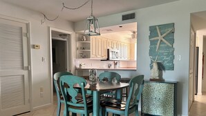 A dining area with a round table and four turquoise chairs, a hanging light fixture, and a decorative starfish wall art piece.