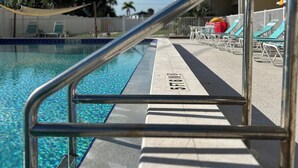 A swimming pool with a metal railing, lounge chairs, and a building in the background.