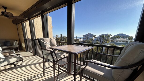 A balcony with a table and chairs, large windows, and a view of palm trees and houses.