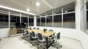 Un salón de conferencias con una larga mesa, sillas, un televisor y ventanas amplias.