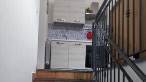 A staircase with a wooden handrail leading to a kitchen area with white cabinets and a blue patterned backsplash. - Magnolia with private parking (Giardini Naxos)