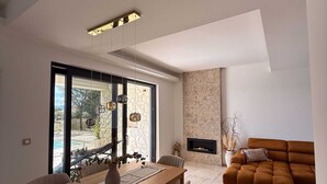 A modern living room with a wooden dining table, beige chairs, a brown sofa, and a fireplace. - Holiday house VILLA AMORA with private pool (Linardići)