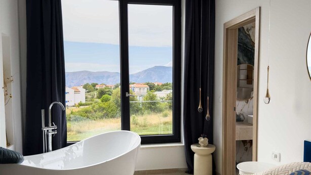 A bedroom with a large bed, a freestanding bathtub, and a view of a mountainous landscape through a large window. - Holiday house VILLA AMORA with private pool (Linardići)