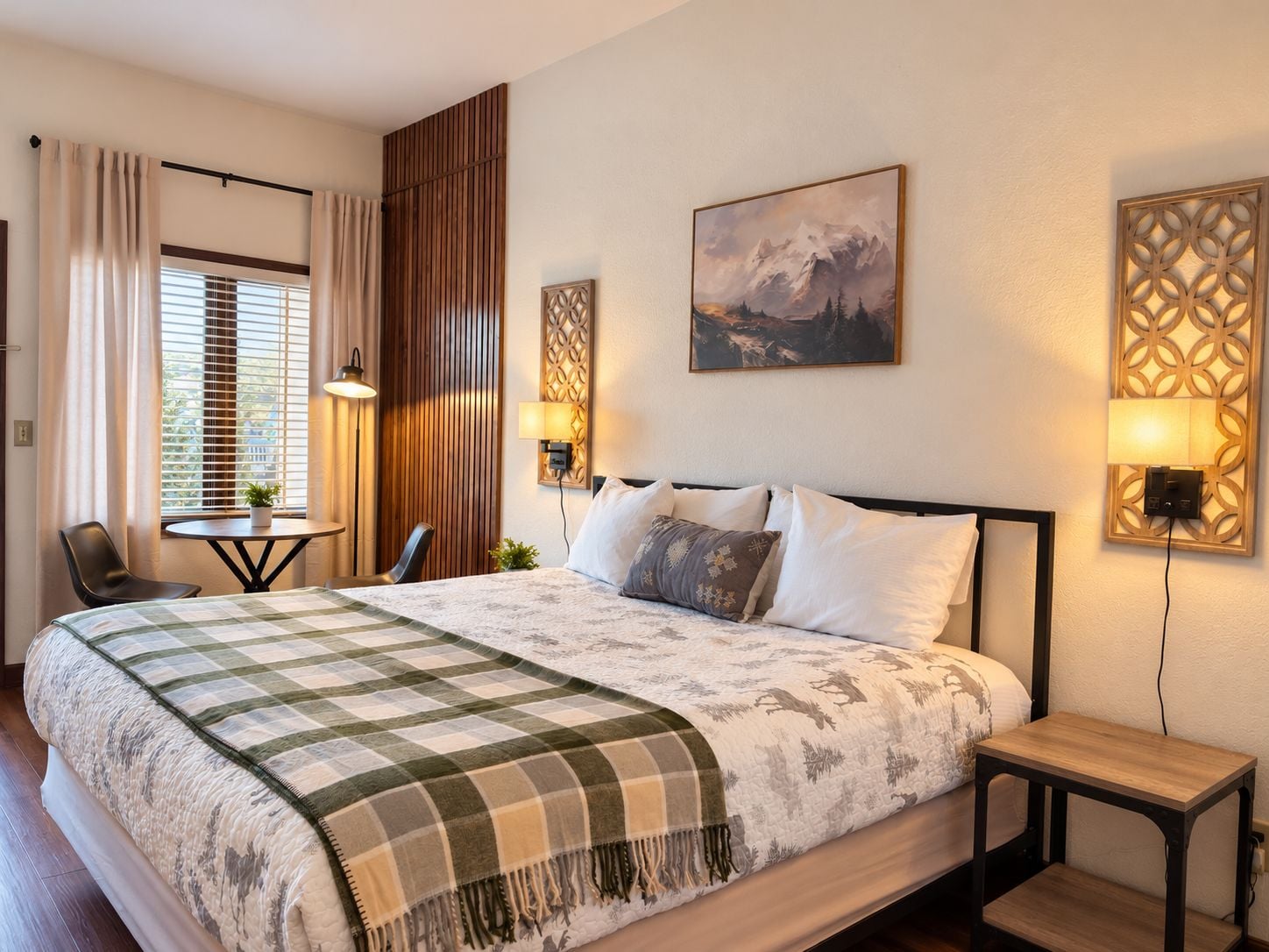 Une chambre d’hôtel avec un lit, des tables de chevet, un bureau, une chaise et une fenêtre avec des rideaux.