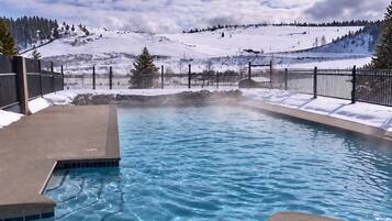 Une piscine à l’eau claire, entourée d’un paysage enneigé et d’une clôture en métal.