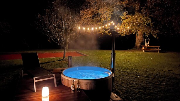 Ein Whirlpool, umgeben von einer Terrasse mit einer Bank und einem Picknicktisch, beleuchtet mit Lichterketten.