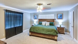 Un dormitorio con una cama de madera, dos mesitas de noche, un ventilador de techo y una ventana con persianas.