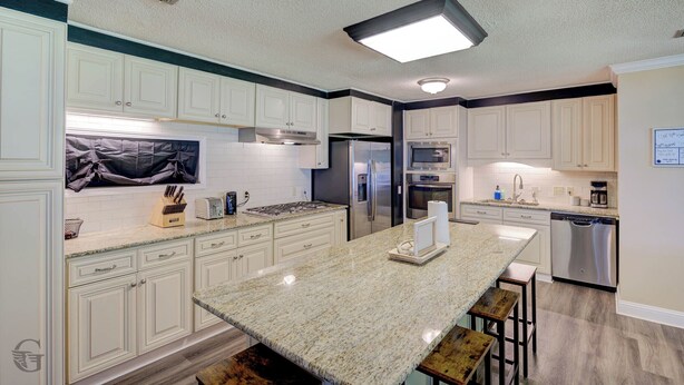 Una cocina moderna con armarios blancos, encimera de granito, electrodomésticos de acero inoxidable y una isla central con taburetes.
