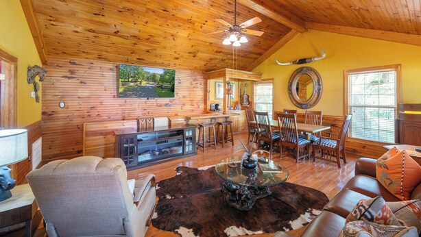 A rustic interior with wooden walls and ceiling, a dining area with a glass-top table, and a bar area. - Charming Cottage on 70 acre Horse Ranch, 14 miles from I-40, Carroll County, TN (Cedar Grove)