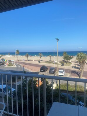 Une vue depuis un balcon donnant sur une plage où sont garées des voitures et où l’on aperçoit des palmiers.