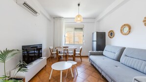 A modern living room with a TV, sofa, dining table, chairs, and a refrigerator.