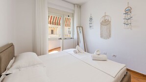 A bedroom with a bed, a window with curtains, a mirror, and wall decorations.