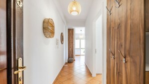A hallway with a wooden door, a woven wall hanging, a textured ceiling light, and a tiled floor.