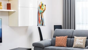 A modern living room with a grey sofa, a black coffee table, and a colorful abstract painting on the wall.