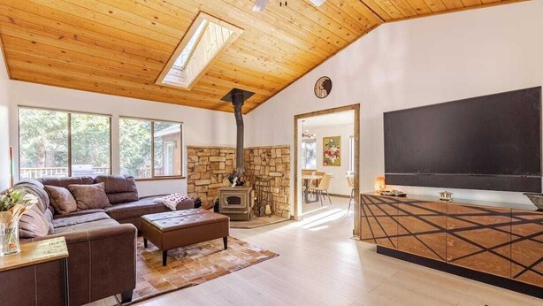 A cozy living room with a stone fireplace, a large TV, and a wooden ceiling.