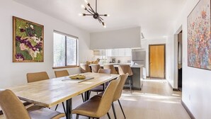 A modern dining area with a long table, several chairs, and a kitchen in the background.