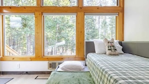 A bedroom with a large window, a bed, a bedside table, and a teddy bear.