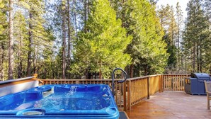 A wooden deck with a hot tub, grill, and seating area surrounded by tall trees.