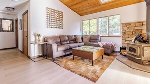 A living room with a wooden ceiling, a stone fireplace, a brown leather sofa, and a coffee table.
