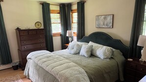 A neatly arranged bedroom with a large bed, a dresser, a bedside table with a lamp, and a framed picture on the wall.