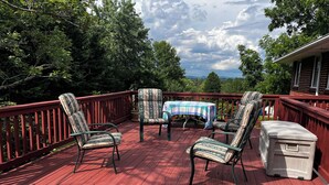 A red deck with four patterned chairs, a table with a checkered tablecloth, and a white cooler.