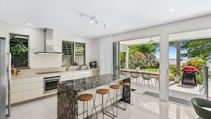 A modern kitchen with a marble island, bar stools, and a view of the outdoors. - Sandveil | Absolute Beachfront Access Home with Pool, Ocean Views & Family Space (Trinity Beach)