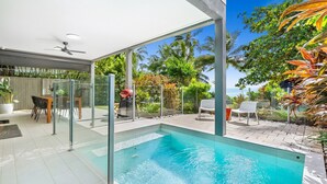 A modern outdoor pool area with a glass enclosure, a barbecue grill, and outdoor seating. - Sandveil | Absolute Beachfront Access Home with Pool, Ocean Views & Family Space (Trinity Beach)