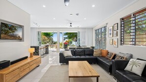 A modern living room with a sectional sofa, a wooden coffee table, and a TV mounted on the wall. - Sandveil | Absolute Beachfront Access Home with Pool, Ocean Views & Family Space (Trinity Beach)